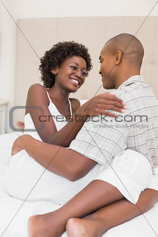 Happy couple sitting on bed cuddling