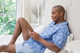 Happy man sitting on bed and texting on phone