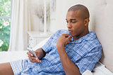 Thinking man sitting on bed and texting on phone
