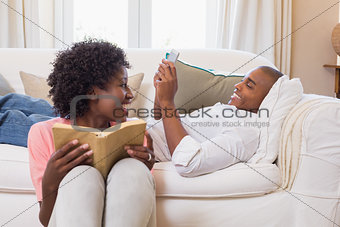 Cute couple relaxing reading book and using smartphone