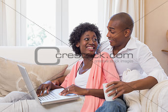 Cute couple relaxing on couch with laptop and coffee