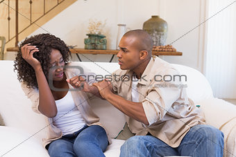 Angry man grabbing his scared partner on sofa
