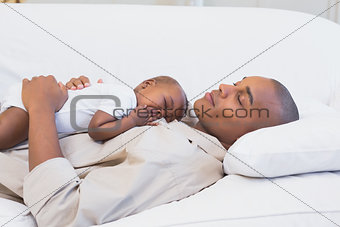Happy young father napping with baby son on couch