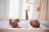 Adorable baby boy lying in his crib playing with mobile
