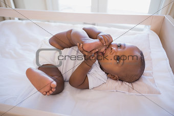 Adorable baby boy lying in his crib chewing foot