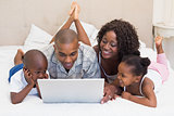 Happy family using laptop together on bed