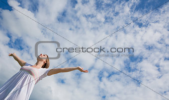 Woman with arms outstretched against blue sky and clouds