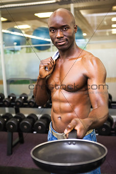 Muscular man holding frying pan in gym