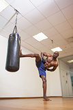 Shirtless muscular boxer kicking punching bag in gym