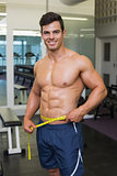 Shirtless muscular man measuring waist in gym