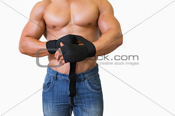 Mid section of a muscular man binds bandage on his hand