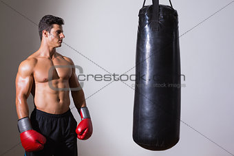 Shirtless muscular boxer looking at punching bag