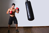 Shirtless muscular boxer with punching bag in gym