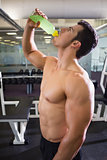 Shirtless muscular man drinking energy drink in gym