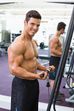Shirtless muscular man using triceps pull down in gym