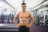 Smiling shirtless muscular man with hands on hips in gym