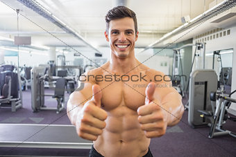 Smiling muscular man giving thumbs up in gym