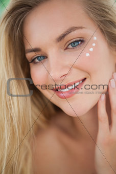 Beautiful natural blonde smiling at camera with eye cream on