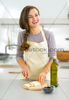 Happy young housewife cutting cheese in kitchen