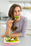 Happy young housewife eating greek salad