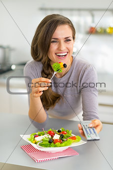 Young woman eating greek salad and watching tv