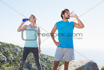 Fit couple standing drinking from water bottles
