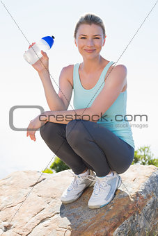 Fit blonde sitting at summit holding water bottle smiling at camera