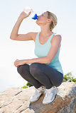 Fit blonde sitting at summit drinking from water bottle