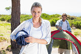 Attractive blonde smiling at camera while partner pitches tent