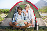 Attractive couple sitting by their tent reading map