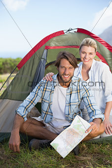 Attractive happy couple sitting by their tent smiling at camera