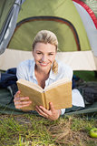 Attractive happy blonde lying in tent holding book