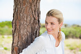 Attractive happy blonde standing by tree