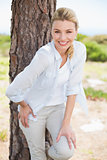 Attractive happy blonde standing by tree smiling at camera