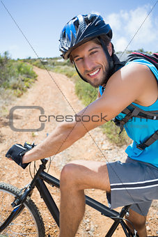 Fit man cycling up mountain trail smiling at camera
