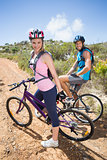 Fit couple cycling up mountain trail smiling