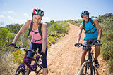 Fit couple cycling down mountain trail smiling at camera