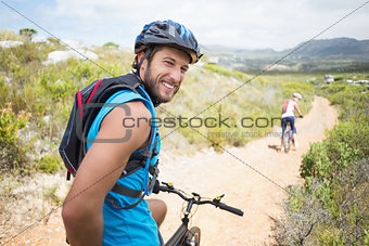 Fit couple cycling on mountain trail man smiling at camera
