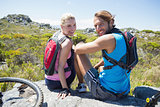 Fit cyclist couple taking a break on rocky peak smiling at camera