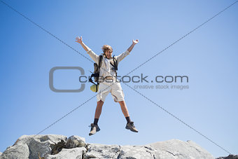 Handsome hiker jumping at the summit smiling at camera