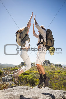 Hiking couple standing on mountain terrain cheering and jumping