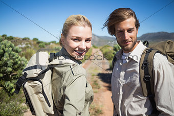 Hiking couple walking on mountain terrain smiling at camera