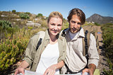 Hiking couple walking on mountain terrain holding map smiling at camera