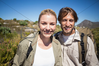 Hiking couple walking on mountain terrain smiling at camera