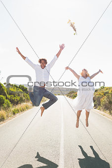 Attractive couple jumping with arms raised on the road