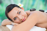 Beautiful brunette enjoying a hot stone massage smiling at camera