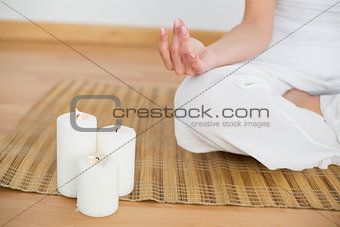 Woman sitting in lotus pose beside white candles