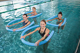 Fitness class doing aqua aerobics with foam rollers