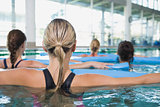 Female fitness class doing aqua aerobics with foam rollers