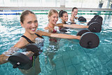 Smiling female fitness class doing aqua aerobics with foam dumbbells